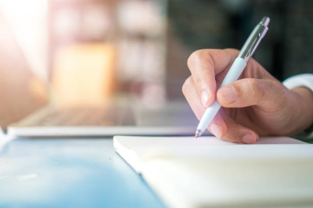 istock Woman hand writing down in small white memo notebook for take a note not to forget or to do list plan for future. 1291872168