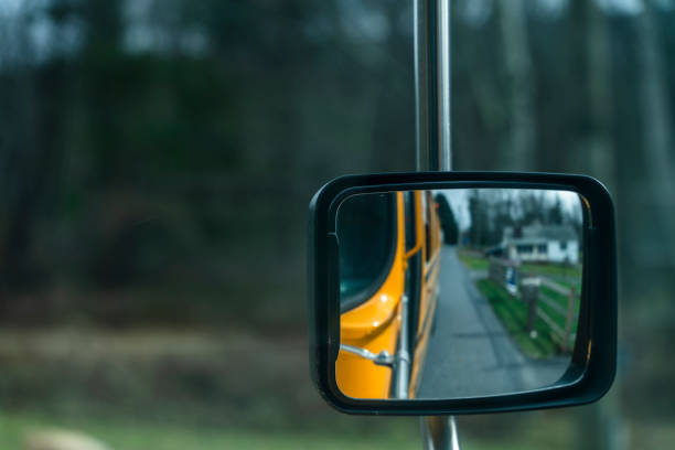 riflesso nello specchietto retrovisore dello scuolabus che guida su una strada in una piccola città alla fine dell'autunno. - driver bus public transportation reflection foto e immagini stock