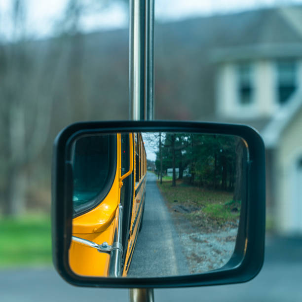 riflesso nello specchietto retrovisore dello scuolabus che guida su una strada in una piccola città alla fine dell'autunno. - driver bus public transportation reflection foto e immagini stock