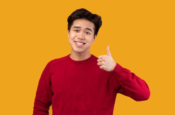 istock Happy asian guy gesturing thumbs up and smiling 1291889422