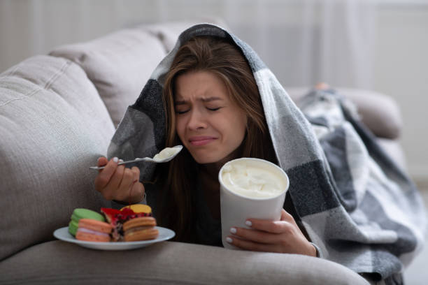 verärgern junge frau umgang mit depressionen durch den verzehr von eis und süßigkeiten unter decke auf dem sofa - bulimia stock-fotos und bilder