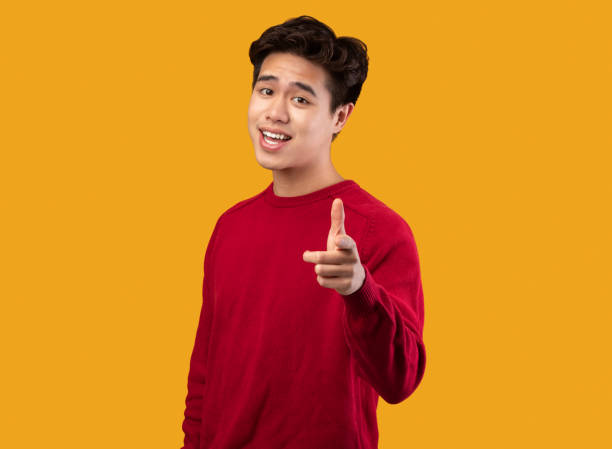 istock Smiling asian guy pointing finger at camera at studio 1291889468