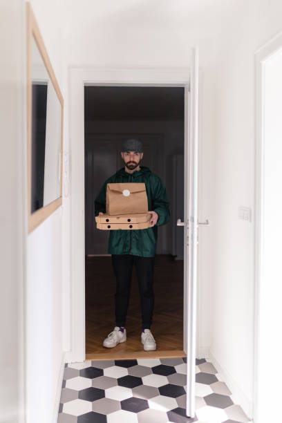 istock Delivery guy in raincoat holding pizza boxes and sealed paper bag on top 1291890573