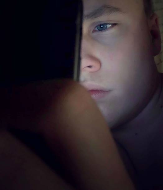 Teenage boy using his mobile phone in the dark. stock photo