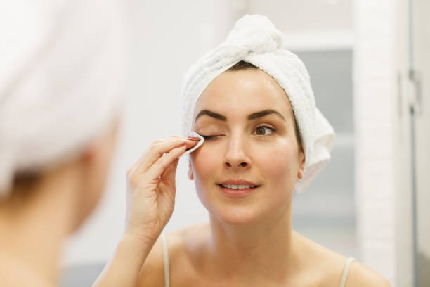 réflexion de la femme dans le miroir de salle de bains, utilisant la serviette sur la tête et enlevant le maquillage d’oeil - démaquillant photos et images de collection