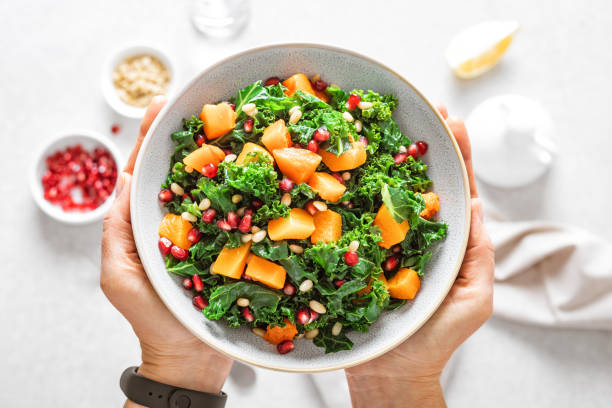 gemüse-salat-schüssel in frauenhänden. frischer grünkohl und gebackener kürbissalat. gesundes ernährungskonzept - superfood stock-fotos und bilder