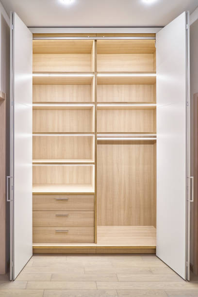 Large lobby wardrobe with LED lighting and white folding doors inner shelves and drawers made of light laminated boards in designed hallway