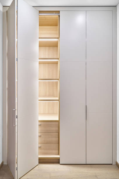 Large lobby wardrobe with LED lighting and white folding doors inner shelves and drawers made of light laminated boards in designed hallway