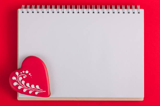 istock Blank white notepad for notes with gingerbread in the form of heart, red office, top view, copy space 1291894988