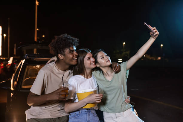 istock Cheerful diverse young friends smiling while taking a selfie together, standing in front of a big screen, ready to watch a movie in an open air cinema 1291900993