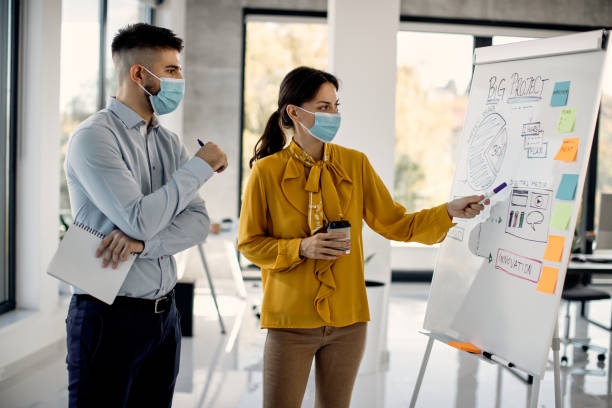 istock Business colleagues wearing face masks while brainstorming about new project on whiteboard in the office. 1291901520