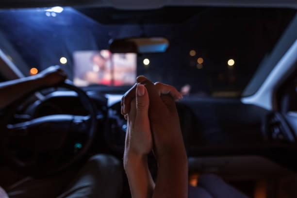 Close up of diverse young couple holding their hands together while having a romantic evening. Young people watching a movie at drive in cinema from the front seats of the car Close up of diverse young couple holding their hands together while having a romantic evening. Young people watching a movie at drive in cinema from the front seats of the car. Entertainment concept film screening photos stock pictures, royalty-free photos & images