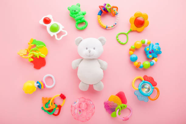 istock Different colorful rattles around white teddy bear on light pink table background. Pastel color. Closeup. Playing toys for baby. Top down view. 1291908248