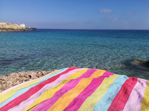 panorama view of the emerald sea of Favignana with colorful beach towel, Sicily, Egadi Islands, Italy