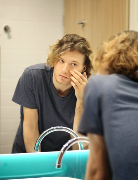 istock young man looking in the mirror,combing his hair,looking at problems on face 1291911543