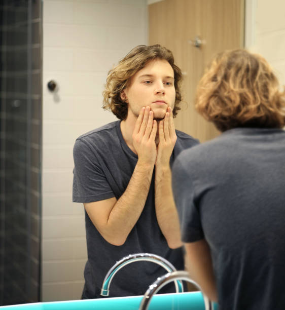 istock young man looking in the mirror,combing his hair,looking at problems on face 1291911544