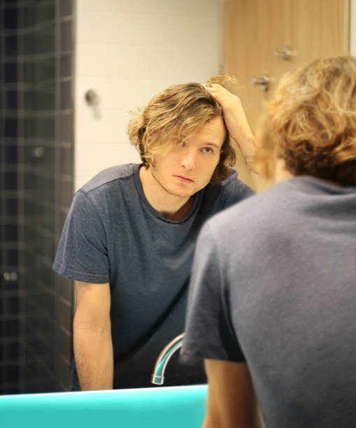 istock young man looking in the mirror,combing his hair,looking at problems on face 1291911551