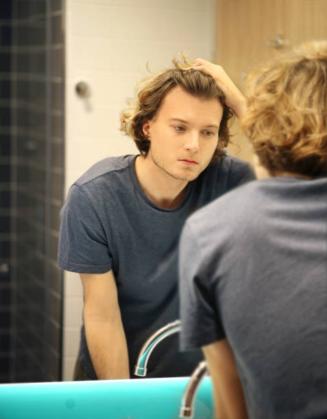 istock young man looking in the mirror,combing his hair,looking at problems on face 1291911557