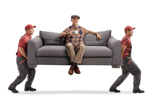 istock Movers carrying an elderly man with a cup of tea seated on a sofa 1291911869
