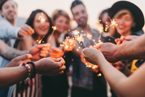 Happy friends holding burning sparklers on rooftop party