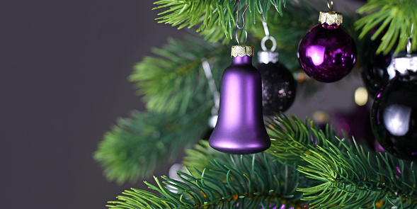 Banner with purple bells haped glass tree bauble on decorated Christmas tree with other seasonal tree ornaments on dark black background