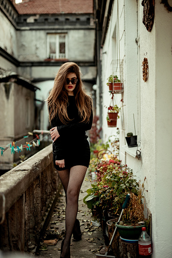 Fashionable elegant young woman wearing a little black dress with long sleeves and sunglasses outdoors in the city on a lovely winter day
