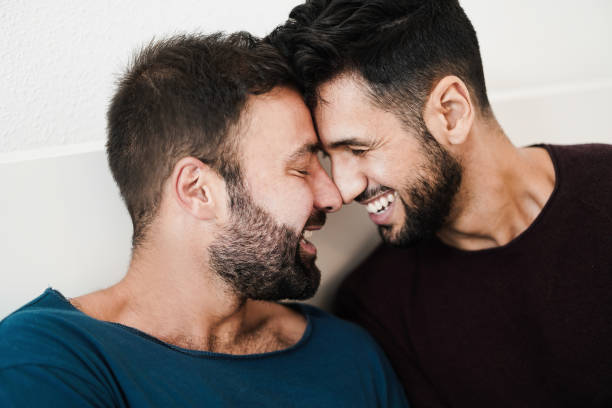 pareja de hombres gay que tienen un momento tierno juntos en casa - homosexual, amor multirracial y concepto de relación - enfoque principal en el ojo del tipo izquierdo - gay man homosexual men kissing fotografías e imágenes de stock