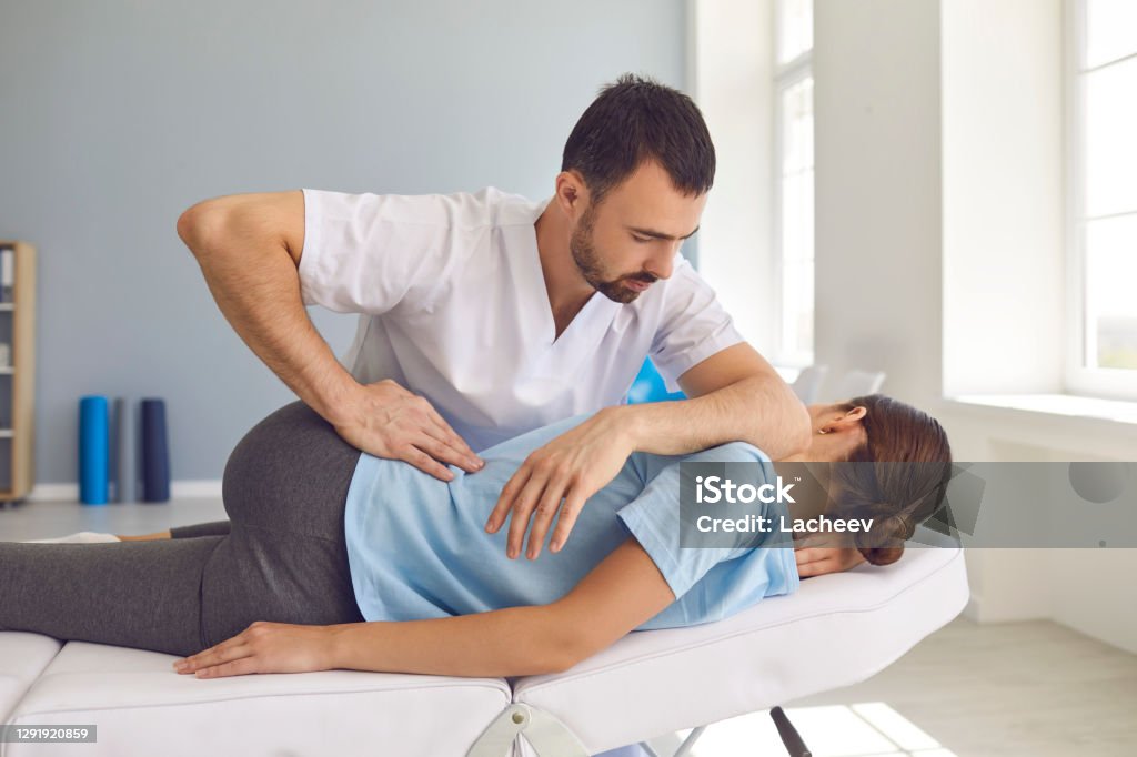 Man doctor chiropractor or osteopath fixing lying womans back in manual therapy clinic Young man doctor chiropractor or osteopath fixing lying womans back with hands movements during visit in manual therapy clinic. Professional chiropractor during work Chiropractic Adjustment Stock Photo