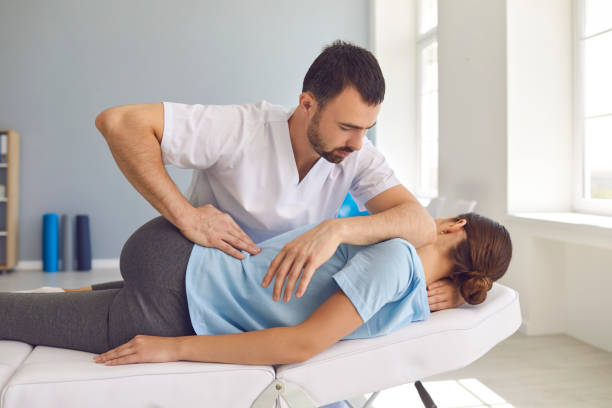 Man doctor chiropractor or osteopath fixing lying womans back in manual therapy clinic Young man doctor chiropractor or osteopath fixing lying womans back with hands movements during visit in manual therapy clinic. Professional chiropractor during work chiropractic adjustment photos stock pictures, royalty-free photos & images