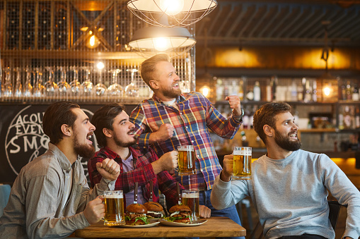 A group of young bearded guys watching sports on tv in a pub bar.