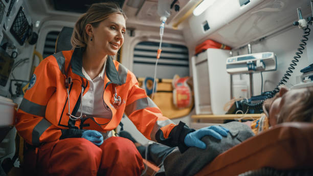 여성 ems 전문 구급대원은 병원으로 가는 길에 부상당한 환자를 위로합니다. 응급 의료 조수는 구급차에서 친절한 방법으로 vinctim의 어깨에 그녀의 손을 넣습니다. - emergency services occupation 뉴스 사진 이미지