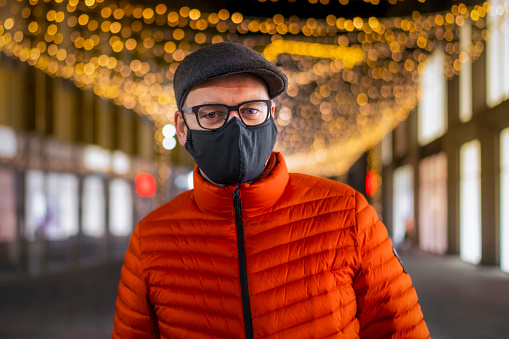Adult man walking the empty streets of the city in Christmas lights enjoying the outdoors wearing protective mask during coronavirus pandemic