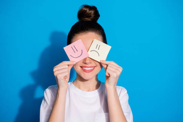 Close-up portrait of her she, nice attractive pretty cheerful girl holding in hands closing eyes two different emotion stickers therapy mood isolated on bright vivid sine vibrant blue color background retrato de cerca de ella ella agradable atractiva chica bastante alegre sosteniendo en las manos cerrando los ojos dos diferentes emociones pegatinas terapia estado de ánimo aislado en el fondo de color azul vibrante sine brillante brillante