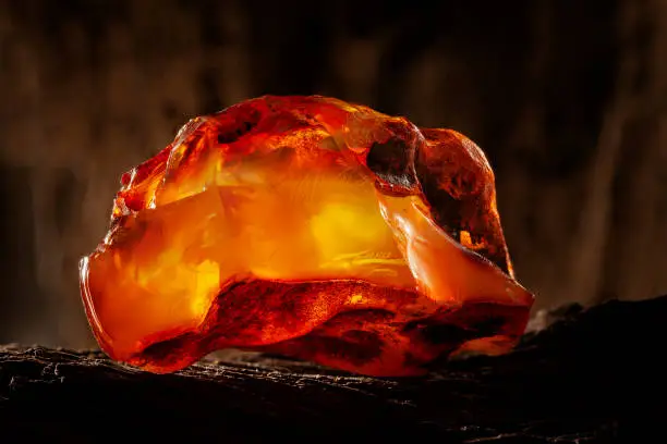 A piece of yellow semi transparent natural amber, classification color honey or cognac, has cracks on its surface. Raw, untached natural shape. Placed on dark stoned wood texture.