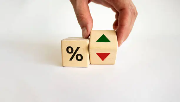 Male hand turns the wooden cubes changes the direction of an arrow symbolizing that the interest rates are going down or vice versa. Business concept. Beautiful white background, copy space.