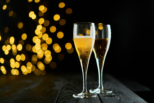 Two glasses of sparkling wine or champagne to celebrate New Year, Merry Christmas, Party or Anniversary with a yellow bokeh effect on dark background.
