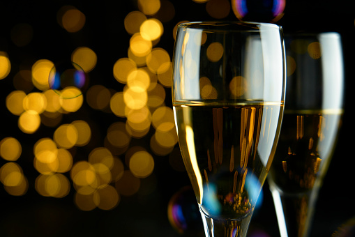 Two glasses of sparkling wine or champagne to celebrate New Year, Merry Christmas, Party or Anniversary with a yellow bokeh effect on dark background.