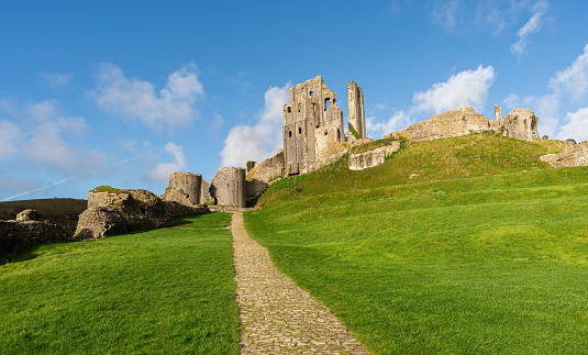 Main cobblestone path leading up to Corfe Castle on a sunny day with bright green grass and no people. Corfe Castle, Wareham, Dorset, England.