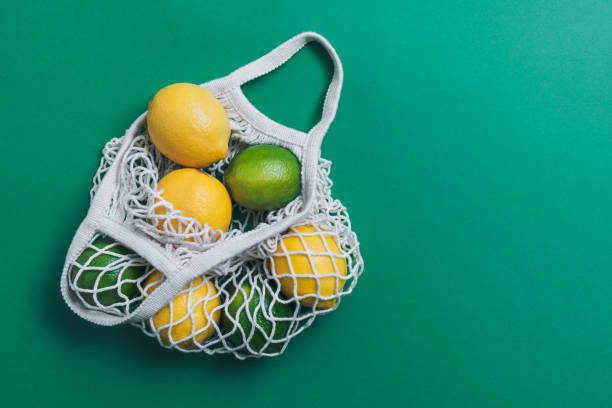 Lemons and limes in mesh bag on green background with copy space