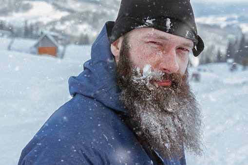 Bearded man in winter, adventure mountain man with a beard in the snow. Background of the old village