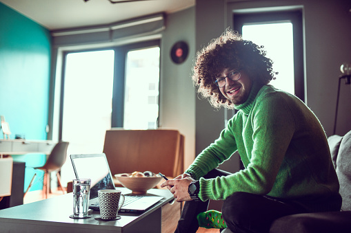 Male In Green Sweatshirt Relaxing At Home With Laptop, Coffee And Using Smartphone