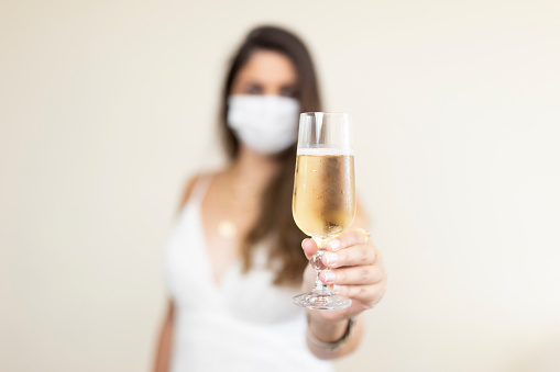 Woman with a protective face mask celebrating with a glass of champagne