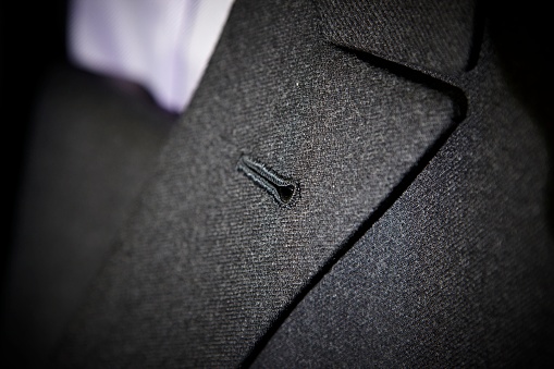 Dark grey formal suit lapel with button hole. Close up.