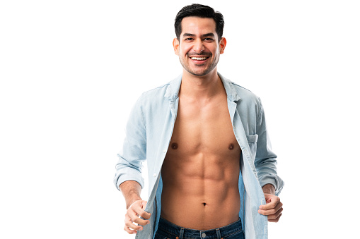 Portrait of a handsome and muscular young man showing off his perfect abs while posing in open shirt against white background