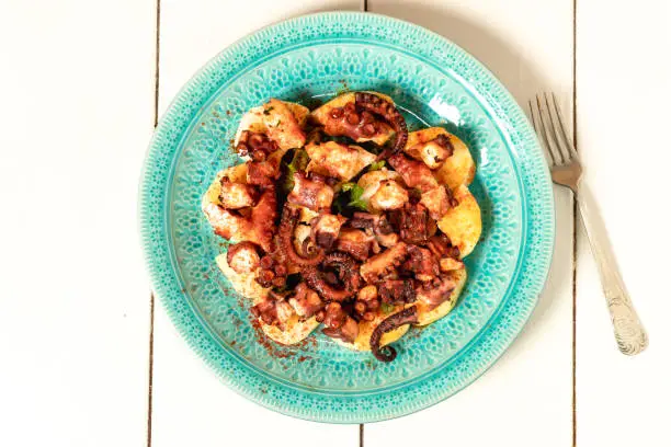 Photo of Turquoise plate with Galician octopus on a white wooden table. Concept healty food.