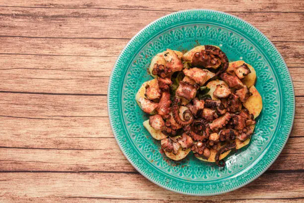 Photo of Turquoise plate with Galician octopus on a wooden table. Concept healty food.