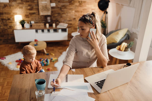 istock Female entrepreneur talking on the phone while being with her son at home. 1291960607