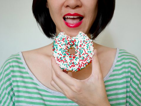 Woman eating white glazed donut with colorful festive sugar strand sprinkles