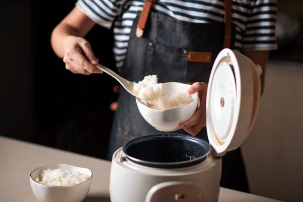 Woman taking out and serving fresh boiled rice from the cooker Woman taking out and serving fresh boiled fragrant jasmine rice from the rice cooker in the kitchen at home serving utensil stock pictures, royalty-free photos & images