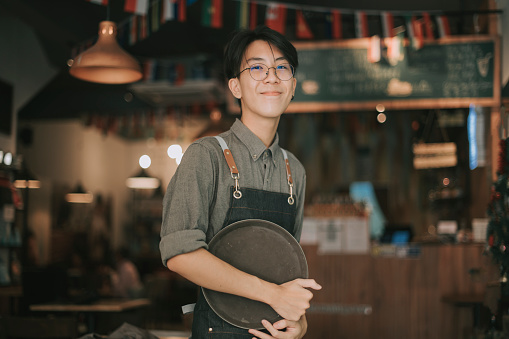 asiático chino adolescente niño camarero mirando a la cámara sonriendo trabajo en la apertura del café photo
